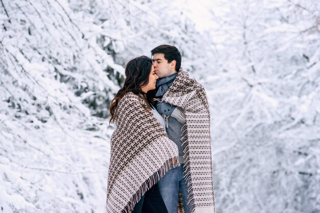 Feliz pareja encantadora cubierta con una manta caliente y caminando en un parque nevado