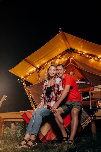 Feliz pareja encantadora relajándose en glamping por la noche cerca de una acogedora hoguera Tienda de campaña de lujo para recreación al aire libre y recreación Concepto de estilo de vida