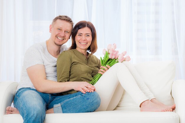 Feliz pareja encantadora sentada en el sofá con ramo sorpresa