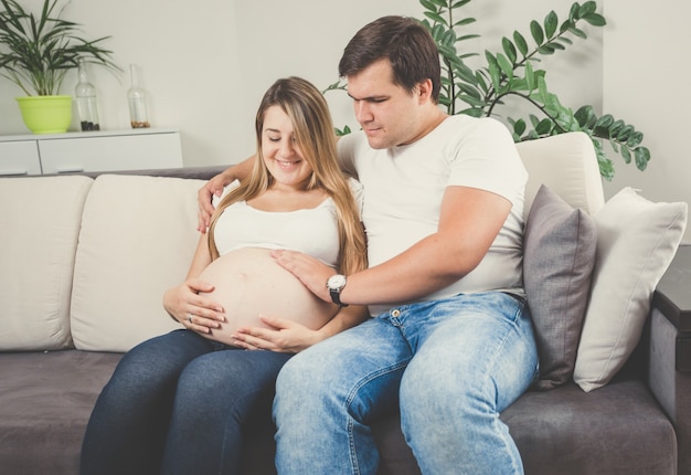 Feliz pareja esperando bebé relajándose en el sofá