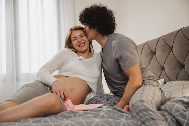 Feliz pareja esperando enamorada disfrutando mientras se relaja en una cama en el dormitorio.