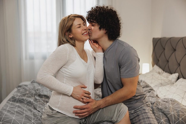 Feliz pareja esperando enamorada disfrutando mientras se relaja en una cama en el dormitorio.