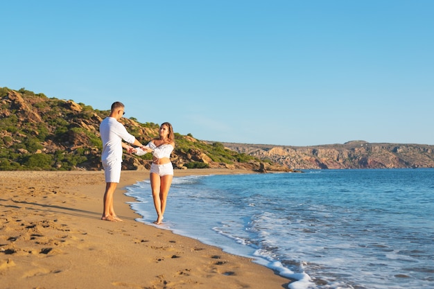 feliz pareja está caminando por la playa durante el atardecer o el amanecer