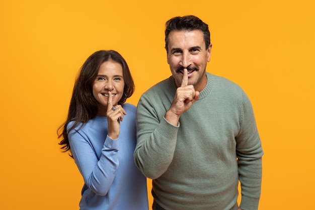 Una feliz pareja europea de ancianos en casual pone el dedo en los labios hace la señal de "shh"