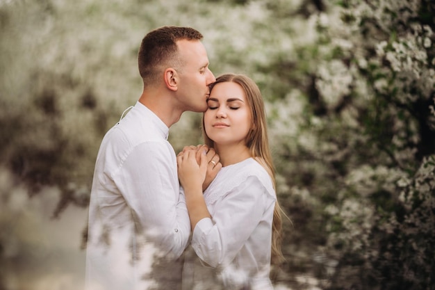 Feliz pareja familiar enamorada en un huerto de manzanos en flor de primavera. La familia feliz se disfruta mientras camina por el jardín. El hombre sostiene la mano de la mujer. Relaciones familiares