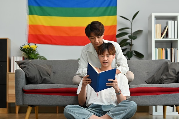 Feliz pareja gay leyendo un libro en un sofá en casa pasando tiempo juntos el fin de semana LGBTQ personas estilo de vida y amor emoción