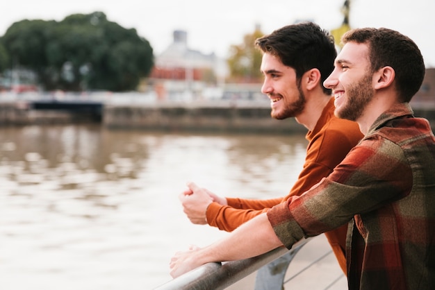 Feliz pareja gay de pie en el terraplén del río