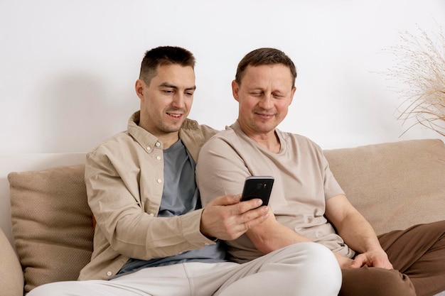 Feliz pareja gay con ropa informal sosteniendo un teléfono inteligente y hablando con amigos en línea con videollamadas Relaciones homosexuales y amor alternativo