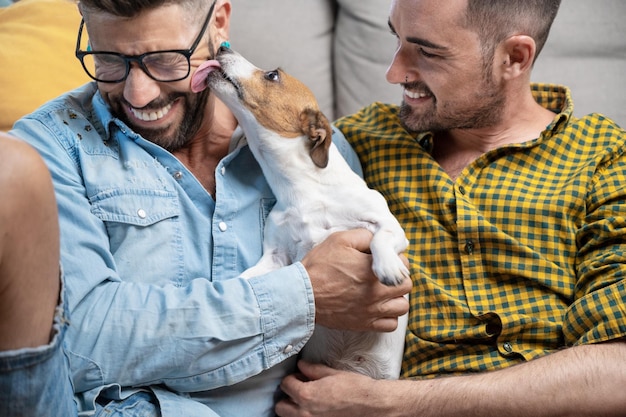 Foto feliz pareja gay sentada en el suelo y jugando con el perro en casa