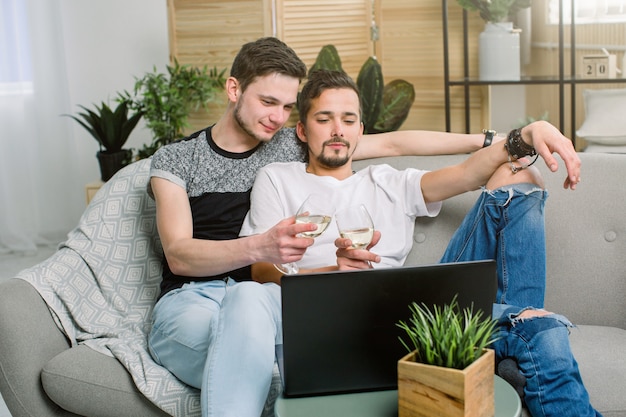 Feliz pareja gay sentado en el sofá, viendo películas y bebiendo vino. Pareja gay, concepto homosexual