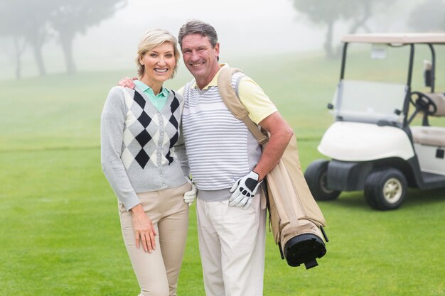 Feliz pareja de golf con buggy de golf detrás