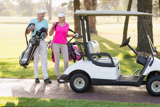 Feliz pareja de golfistas maduros por buggy de golf