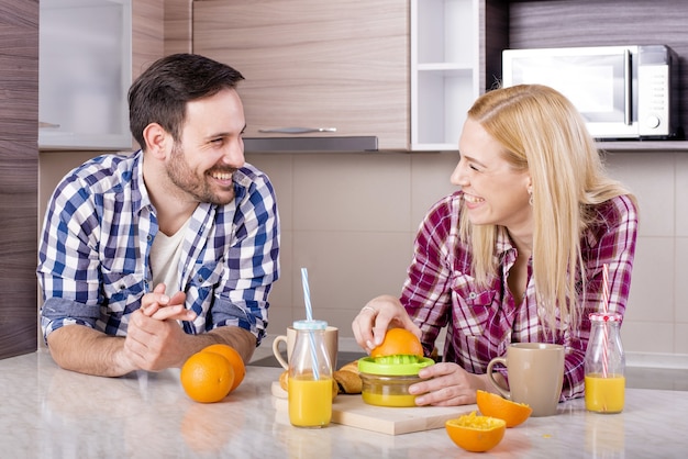 Feliz pareja haciendo jugo de naranja natural en la cocina y disfrutando de su tiempo