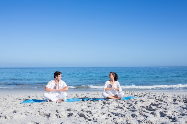 Feliz pareja haciendo yoga junto al agua en la playa