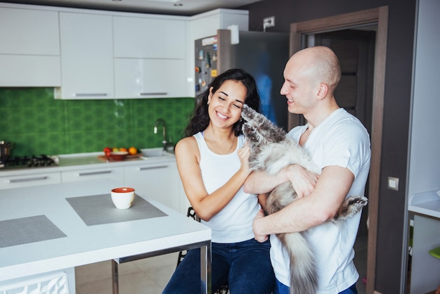 Feliz pareja hermosa joven itting en cocina gato sonriendo.