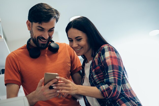 Feliz pareja hermosa con ropa informal mirando la pantalla del teléfono inteligente y sonriendo