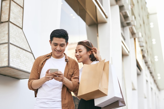 Feliz pareja hermosa usando teléfonos inteligentes y comprando juntos.