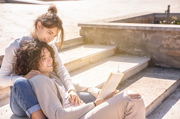 Feliz pareja heterosexual joven sonriendo y leyendo el libro al aire libre