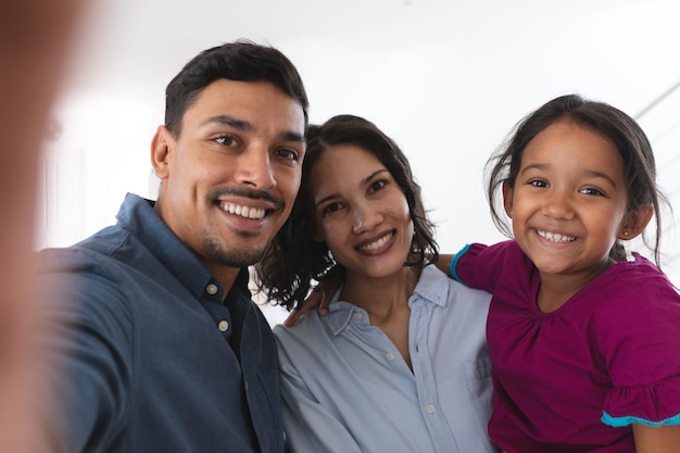 Foto feliz pareja hispana e hija tomándose selfie sonriendo a la cámara. en casa aislado durante el cierre de cuarentena.