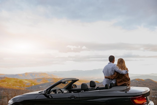 Foto feliz pareja hombre y mujer disfrutando de hermosas vistas viajando en cabriolet mirando montañas