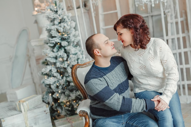 Feliz pareja hombre y mujer en suéteres en invierno en una habitación decorada en previsión del año nuevo