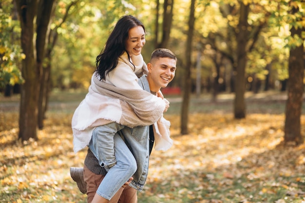 Feliz pareja hombre sosteniendo a una mujer a sus espaldas y divirtiéndose juntos en el parque de otoño