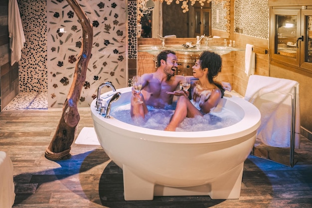 Feliz pareja interracial relajada en el jacuzzi disfrutando y bebiendo vino xA