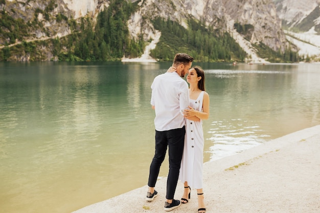 Feliz pareja joven abrazándose y sonriendo mientras está de pie cerca del lago Braies, Italia