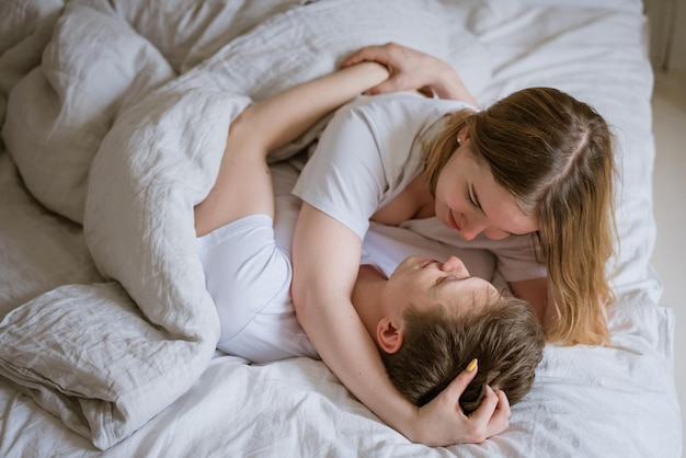 Feliz pareja joven se acuesta en la cama y se abrazan con ropa de cama blanca