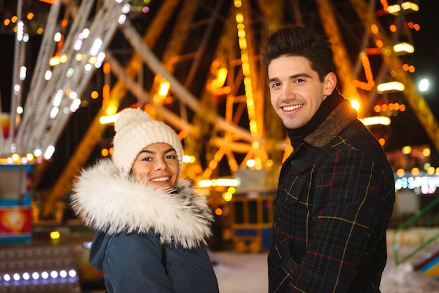 Feliz pareja joven alegre divirtiéndose en el parque de patinaje sobre hielo por la noche