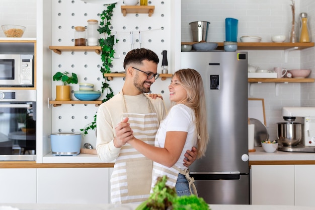 Foto feliz pareja joven alegre padres de familia bailando juntos en la cocina preparando comida para una cena romántica pasando tiempo juntos
