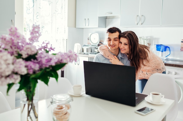 Feliz pareja joven auto aislado en casa usando laptop tomando café