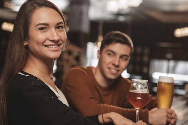 Feliz pareja joven bebiendo cerveza en una cita en el bar