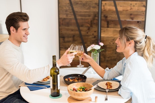 feliz pareja joven brindando con vino y cenando en casa