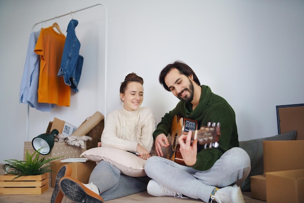 Feliz pareja joven con cajas y guitarra en piso nuevo, nuevo hogar y concepto de reubicación.