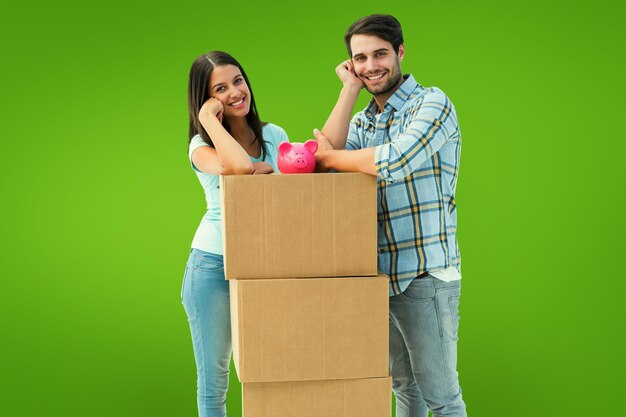 Feliz pareja joven con cajas de mudanza y hucha contra viñeta verde