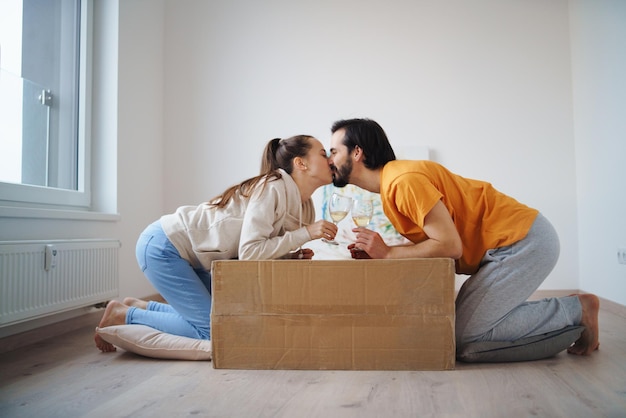 Feliz pareja joven con cajas y vino en piso nuevo, nuevo hogar y concepto de reubicación.