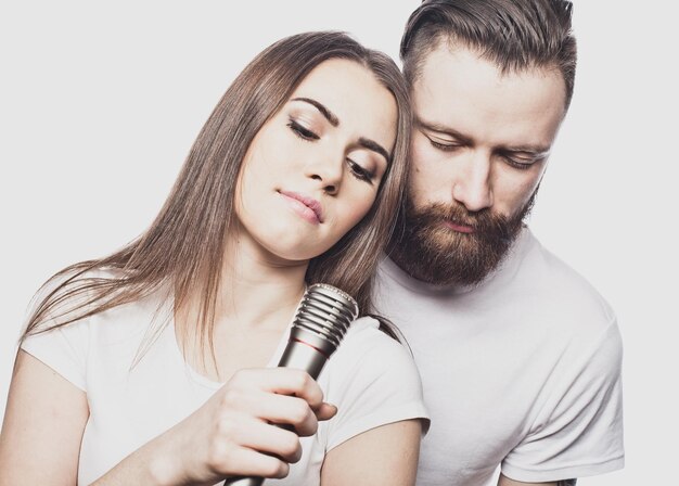 Feliz pareja joven cantando en karaoke sobre fondo blanco.