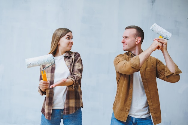 Feliz pareja joven casada enamorada en camisas haciendo renovaciones renovando paredes pintando con rodillo de pintura blanca preparándose para mudarse a una nueva casa enfoque selectivo