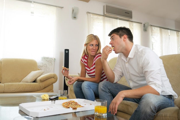 feliz pareja joven come pizza fresca en casa relajándose y viendo televisión