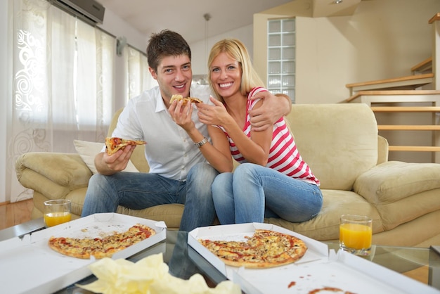 feliz pareja joven come pizza fresca en casa relajándose y viendo televisión