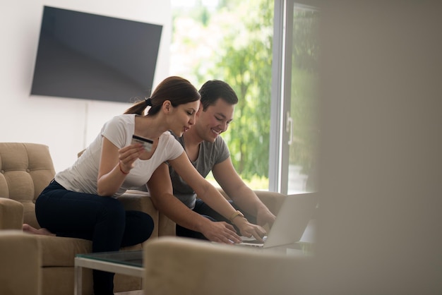 feliz pareja joven comprando en línea usando una computadora portátil y una tarjeta de crédito en su villa de lujo