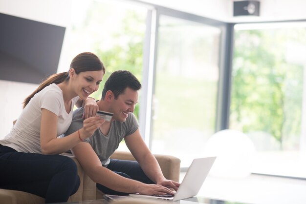 feliz pareja joven comprando en línea usando una computadora portátil y una tarjeta de crédito en su villa de lujo