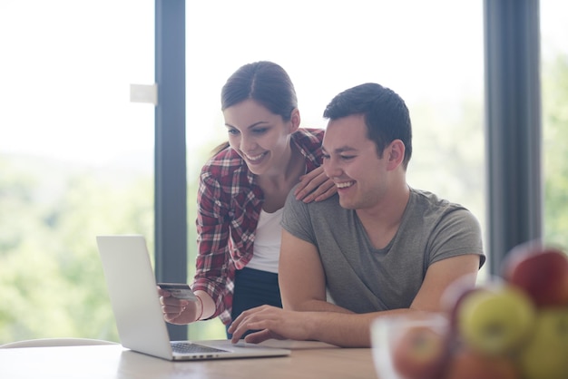 feliz pareja joven comprando en línea usando una computadora portátil y una tarjeta de crédito en su villa de lujo