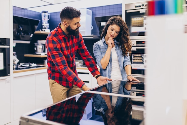 Foto feliz pareja joven comprando placa de cocina eléctrica en la tienda.