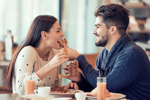 Feliz pareja joven desayunando en la cafetería