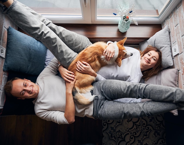 Feliz pareja joven descansando en el asiento de la ventana con un lindo perro