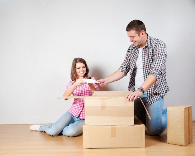 Feliz pareja joven desempacando o empacando cajas y mudándose a un nuevo hogar.