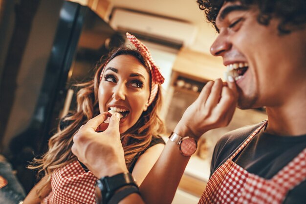 Feliz pareja joven disfruta y se divierte comiendo rebanadas de manzana y haciendo comida saludable juntos en la cocina de su casa.