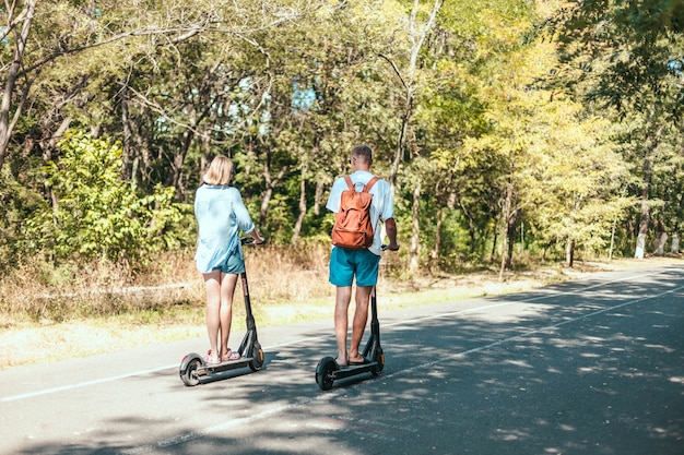 Feliz pareja joven disfrutando juntos mientras conduce scooters eléctricos en el parque de la ciudad